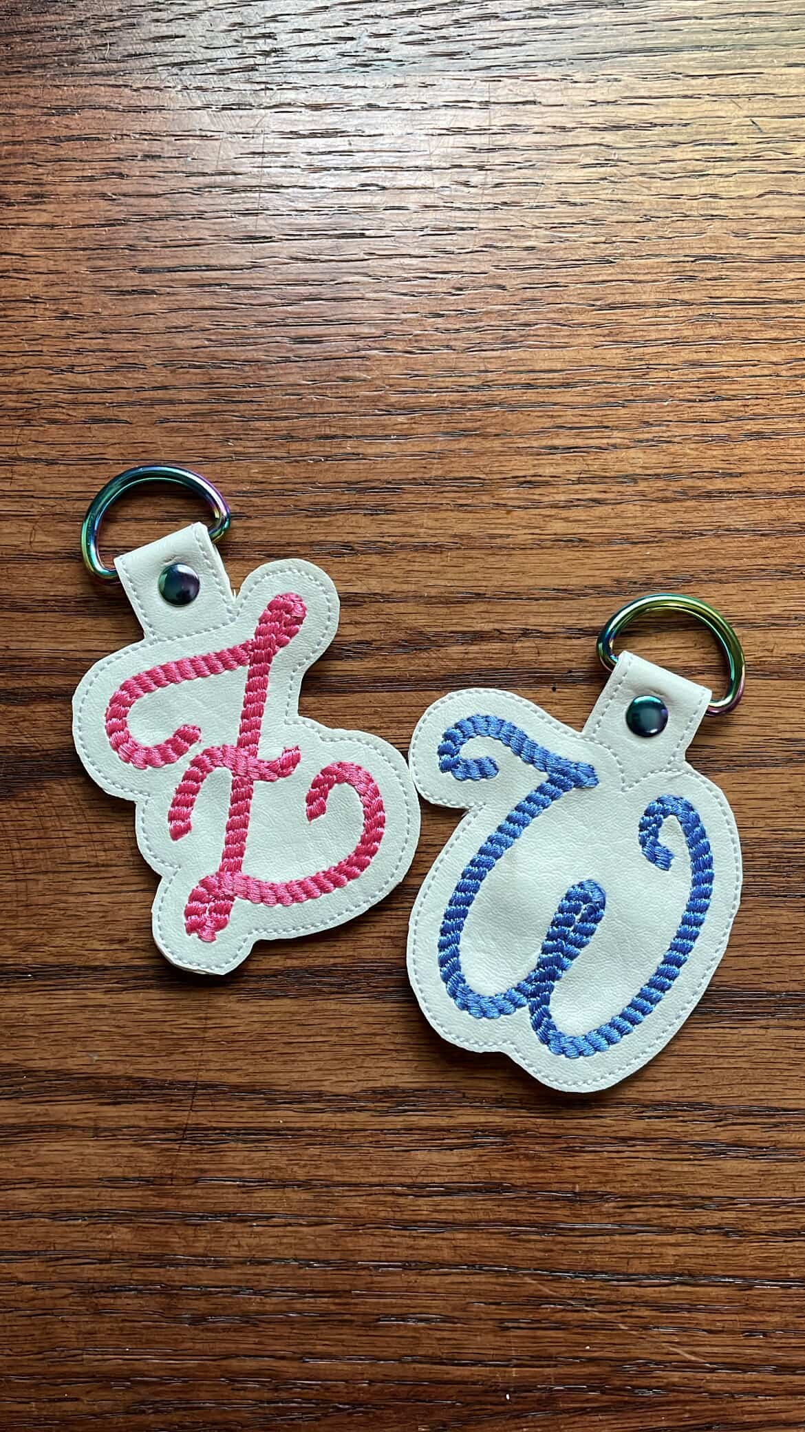 Two keychains with embroidered letters 'f' and 'q' on a wooden surface.