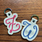 Two keychains with embroidered letters 'f' and 'q' on a wooden surface.